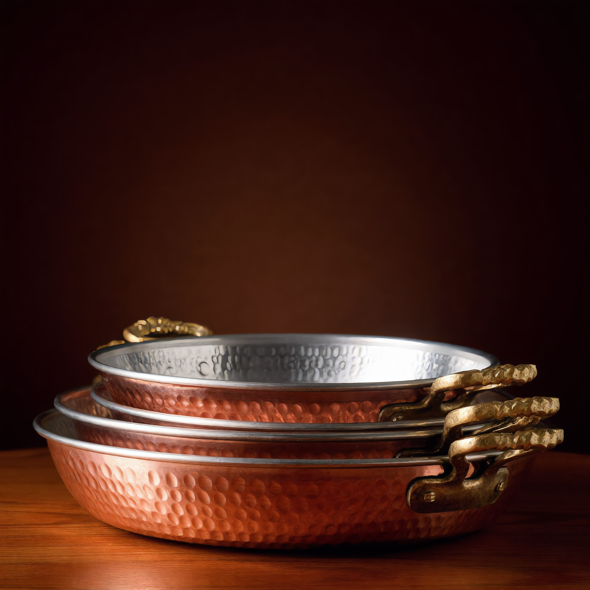 Four nested copper pans with ornate brass handles, Cuivra