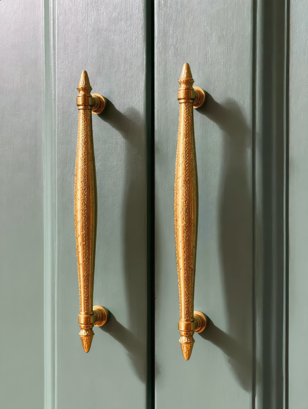 Two brass handles on sage green cabinet doors