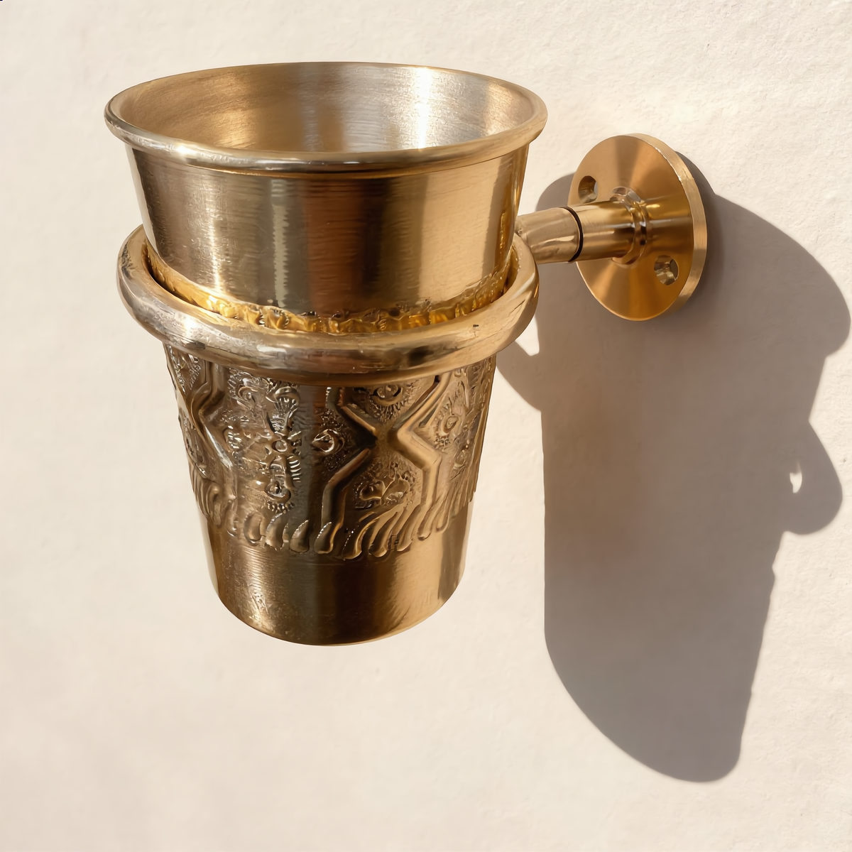 Wall-mounted brass toothbrush cup holder on a cream wall