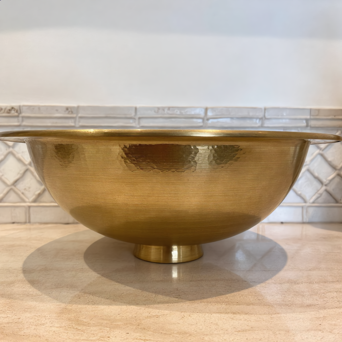 Hammered brass vessel sink on a travertine bathroom counter, side view, Cuivra