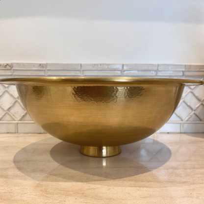 Hammered brass vessel sink on a travertine bathroom counter, side view, Cuivra