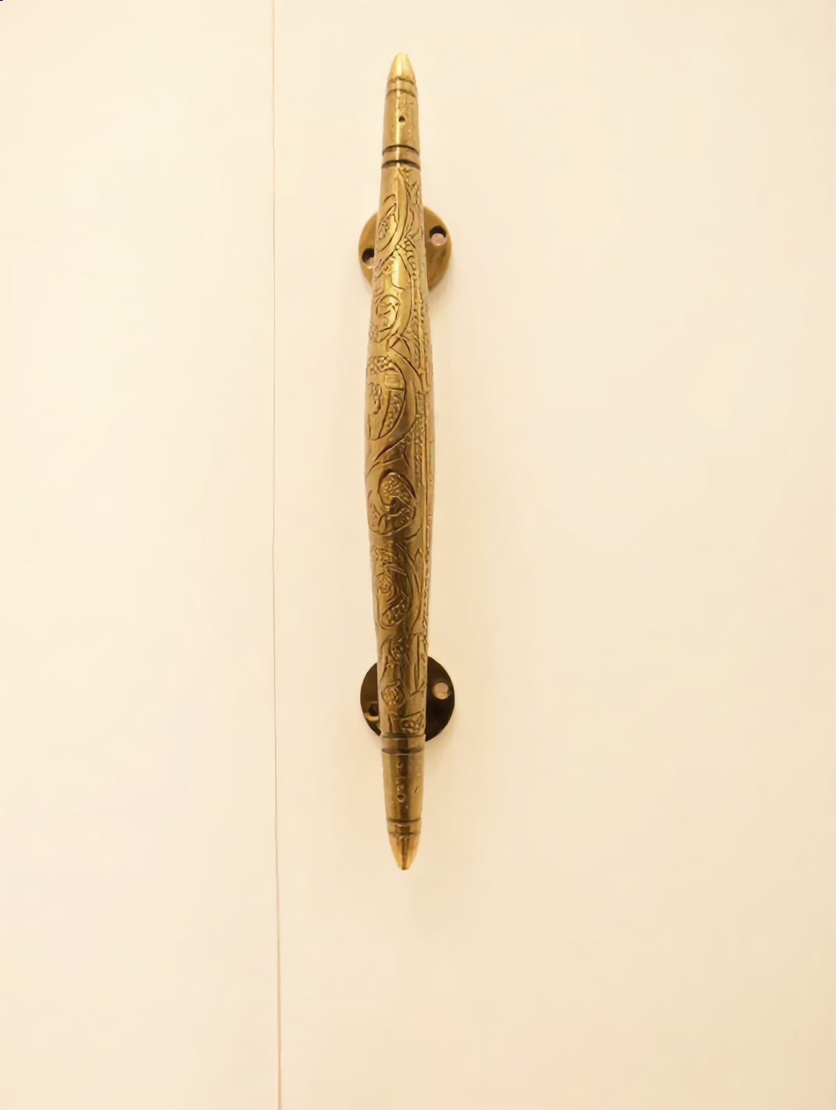 Engraved Moroccan brass cabinet handle on a cream wardrobe door, Cuivra