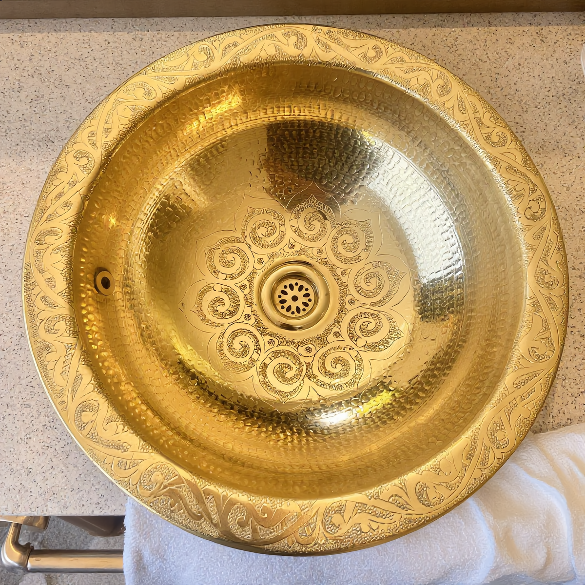Hand-engraved Moroccan brass vessel sink on a travertine vanity, top view, Cuivra