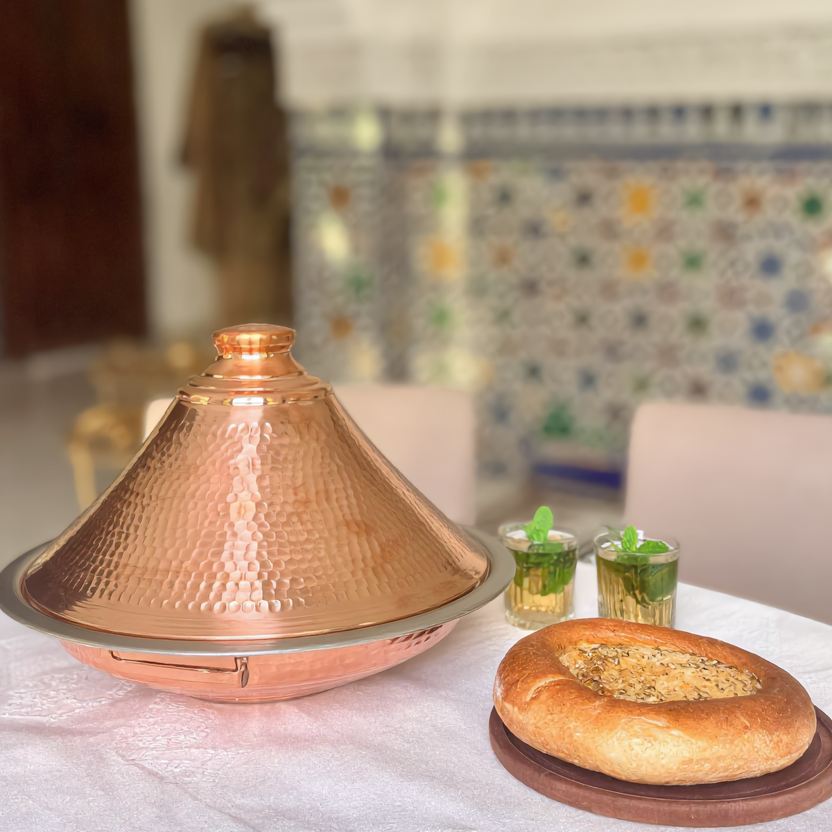 Dyafa hand-hammered red copper tajine on a Moroccan table with bread and mint tea, Cuivra